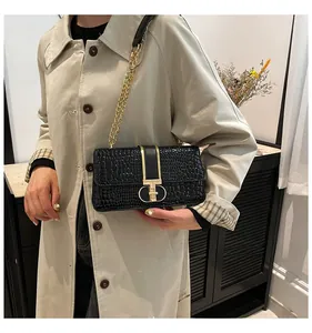 Detail of black crocodile embossed shoulder bag featuring a gold T-lock and chain strap