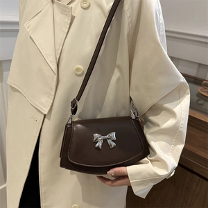 Elegant dark brown leather saddle bag with silver bow buckle on white trench coat