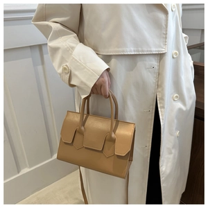 Detail of camel leather handbag with pointed straps held by model in trench coat