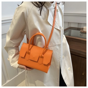 Detail of bright orange leather handbag styled with a beige trench coat for autumn fashion