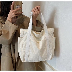 Detail of cream corduroy tote bag featuring golden metal buckle and side pocket texture
