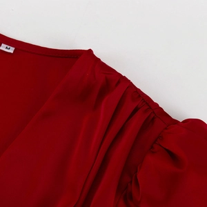 Détail de robe en satin rouge avec manches bouffantes plissées et décolleté en V