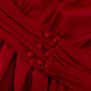Détail de la taille d'une robe en satin rouge avec plis et boutons recouverts de tissu