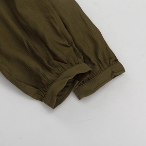 Détail des poignets plissés et du tissu texturé vert olive sur une robe à manches longues