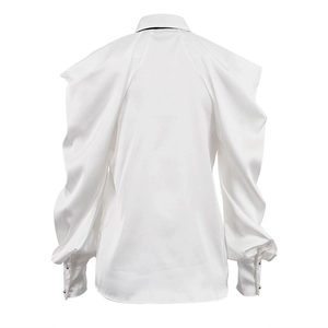 Dettaglio camicia di raso bianco con maniche a sbuffo e polsini abbottonati sul retro