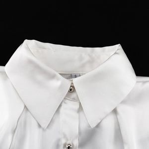 Dettaglio del colletto di camicia in raso bianco con bottoni argento lucidi e risvolto