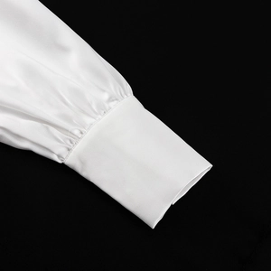 Dettaglio del polsino in raso bianco con eleganti arricciature e finitura lucida