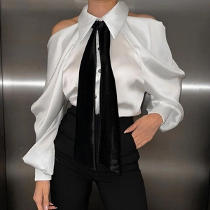 Dettaglio camicia in raso con spalle scoperte, maniche a sbuffo e accessorio cravatta nera