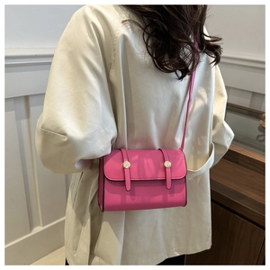 Détail du sac bandoulière rose avec clous dorés et lanières sur un trench-coat