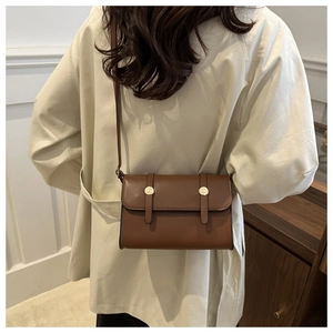 Sac bandoulière en cuir marron avec boucle dorée porté par un mannequin dans un intérieur