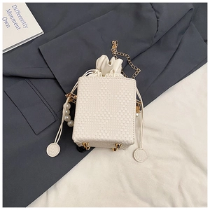 Detail of cream woven bucket bag with pearl handle, gold chain and protective metal feet