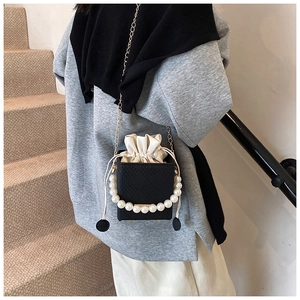 Detail of black box bag featuring white pearl handle, gold chain and drawstring lining