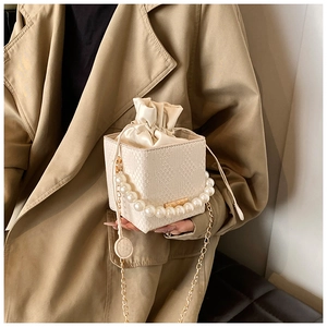 Detail of pearl handle handbag with woven texture and gold chain strap on trench coat