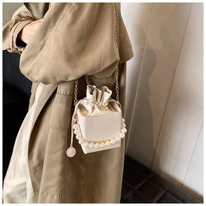 Detail of cream bucket bag featuring pearl handle, gold chain strap, and woven texture