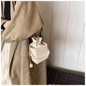 Detail of white mini bucket bag with pearl handle, chain strap, and drawstring closure