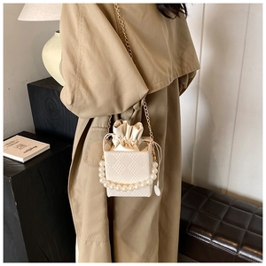 Detail of cream bucket bag showing quilted texture, pearl handle and drawstring closure
