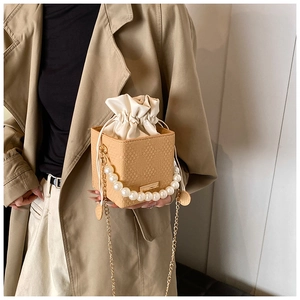 Detail of beige woven box bag with faux pearl handle and gold chain strap on a trench coat