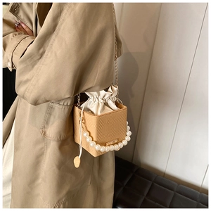Detail of pearl handle and drawstring closure on apricot bucket bag with chain strap