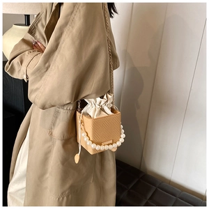 Dettaglio borsa a secchiello beige con manico di perle, trama intrecciata e catena