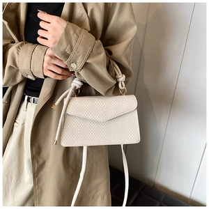 Borsa a tracolla beige chic con trama intrecciata indossata con un trench kaki