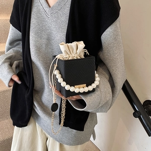 Chic black bucket bag with pearl handle and gold chain strap shown on model