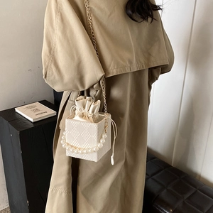 Elegant pearl handle cream bucket bag with gold chain strap worn over a khaki trench coat