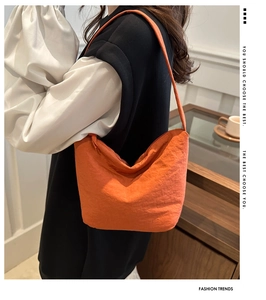 Side view of orange pleated shoulder bag with textured fabric on a female model