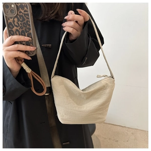 Shoulder view of a beige minimalist nylon hobo bag featuring subtle pleated textures