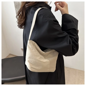 Minimalist cream canvas shoulder bag with pleated texture shown on model in black coat