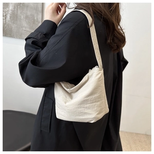 Modern beige nylon shoulder bag shown worn by a model in a minimalist indoor setting