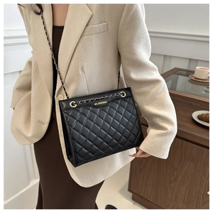 Detail of black quilted leather shoulder bag with gold chain strap worn by a model