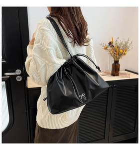 Detail of black pleated shoulder bag with metal bow logo worn with white cable knit sweater