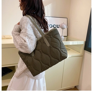 Side view of olive green quilted puffer tote bag on model in a minimalist interior