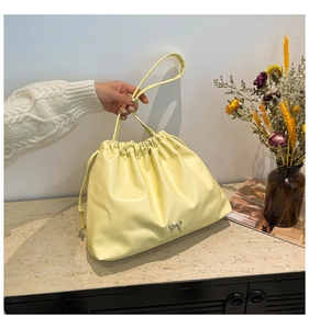 Detail of light yellow leather drawstring bag with delicate silver bow and long strap
