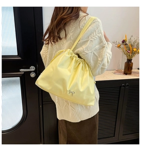 Detail of light yellow drawstring shoulder bag with metallic bow charm and soft texture