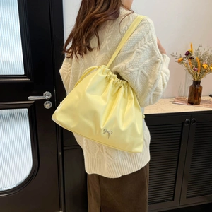 Large pale yellow drawstring tote bag with silver bow accent worn over the shoulder
