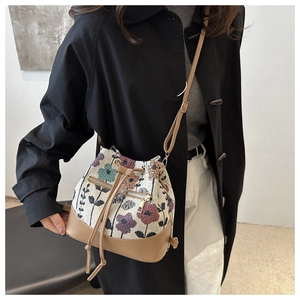 Ethnic bucket bag with floral patterns and leather straps worn by a model in a studio