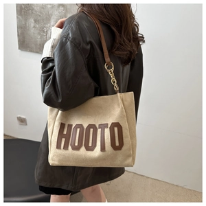 Detail of HOOTO beige suede tote bag featuring brown letters and gold chain strap