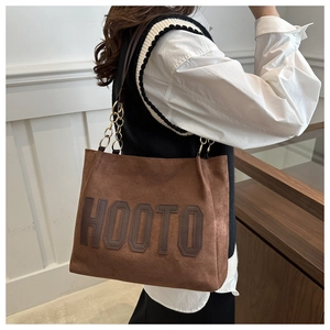 Detail of brown suede tote bag featuring HOOTO lettering and gold chain straps