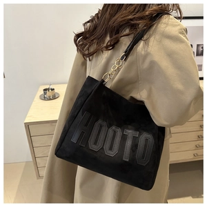 Detail of black suede tote bag featuring HOOTO applique and gold chain strap accents