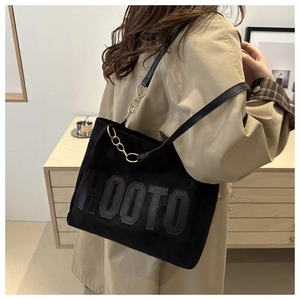 Detail of black suede tote bag featuring a HOOTO logo and chain strap on a khaki coat