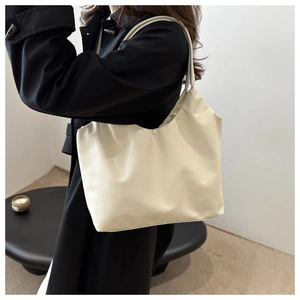 Close-up of minimalist cream-white PU leather tote bag on model shoulder with black coat