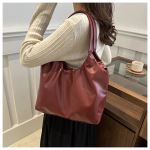 Detailed view of deep red pleated tote bag made of PU leather worn on shoulder