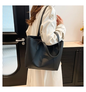Detail shot of a black leather tote bag worn with a white trench coat in an urban setting