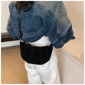 Détail du sac croissant plissé noir porté à l'épaule par un mannequin en intérieur