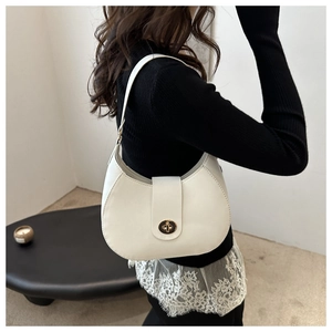 Detail shot of a white half-moon shoulder bag featuring a gold oval twist-lock closure