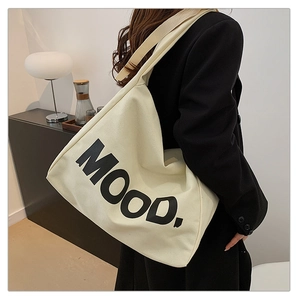 Dettaglio di una grande borsa tote in tela beige con scritta MOOD indossata da una modella