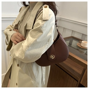 Close-up of brown leather crescent underarm bag with gold metal clasp on a model