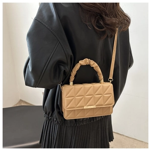 Close-up of quilted khaki crossbody bag with pleated handle on a model in leather jacket