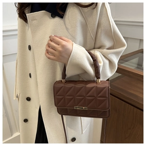 Detail of dark brown quilted crossbody bag with gold buckle on a model in wool coat